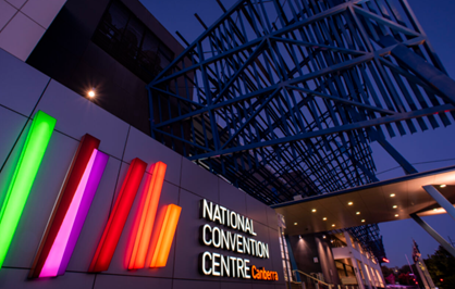 Exterior of National Convention Centre at dusk, with multicolored vertical light tubes beside its sign.