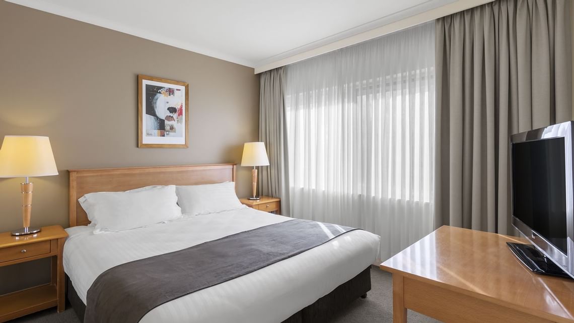 Hotel room with a king-size bed, two wooden nightstands, and warm lamps on both sides.